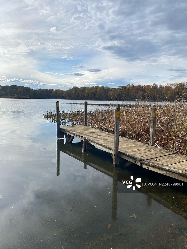 秋季树木环绕的宁静湖泊，带有木制码头，天空多云，美国，阿尔比恩图片素材