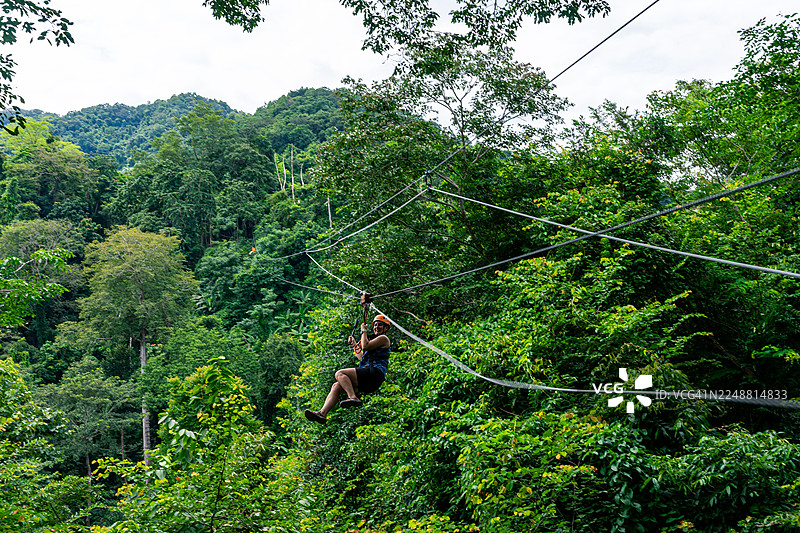 女子在老挝光西瀑布探险旅行，在郁郁葱葱的热带雨林树冠中体验高空滑索，在积极的假期中感受自由与兴奋图片素材