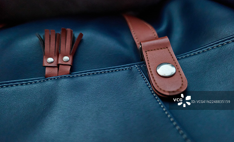 深蓝色皮包特写，带有棕色肩带和银色铆钉图片素材