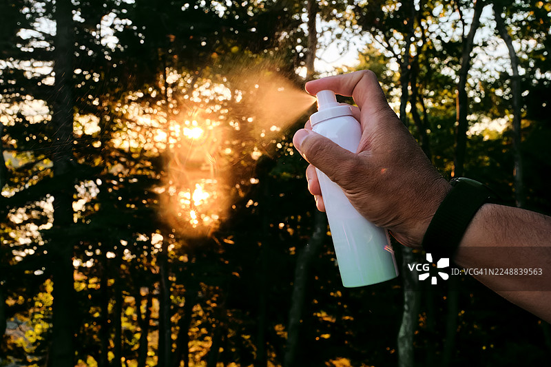一只手在针叶林背景下喷射气雾罐。图片素材