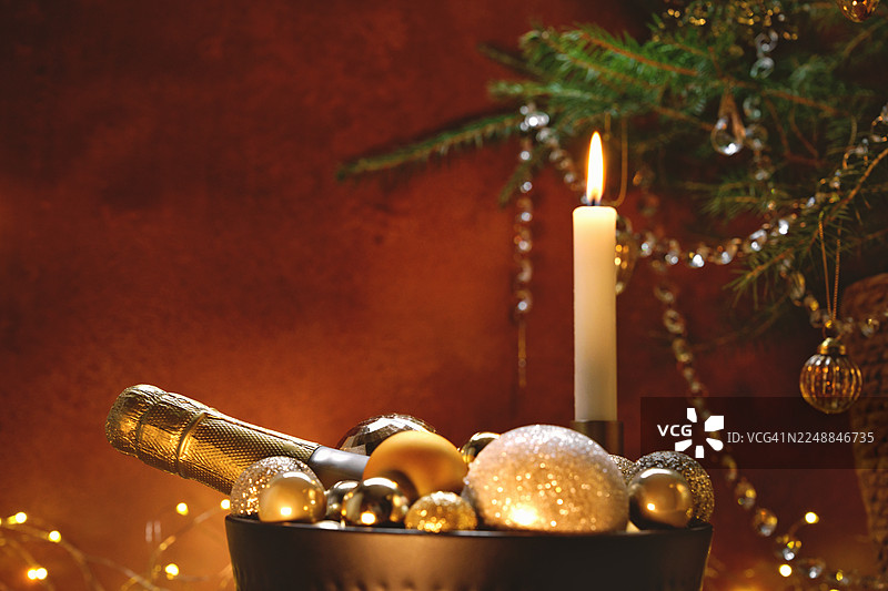 装在碗里的起泡酒瓶，旁边有圣诞装饰球、燃烧的蜡烛和香槟杯，桌上放着篮子里的圣诞树和装饰球。图片素材