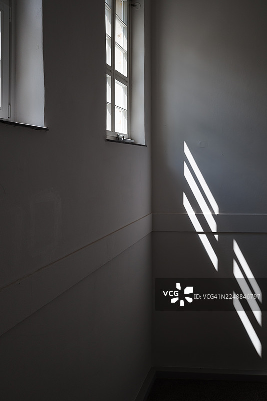 明亮的自然光透过窗户照射进房间的角落，在纯白色的墙壁上投射出锐利的斜线和几何阴影图案。图片素材