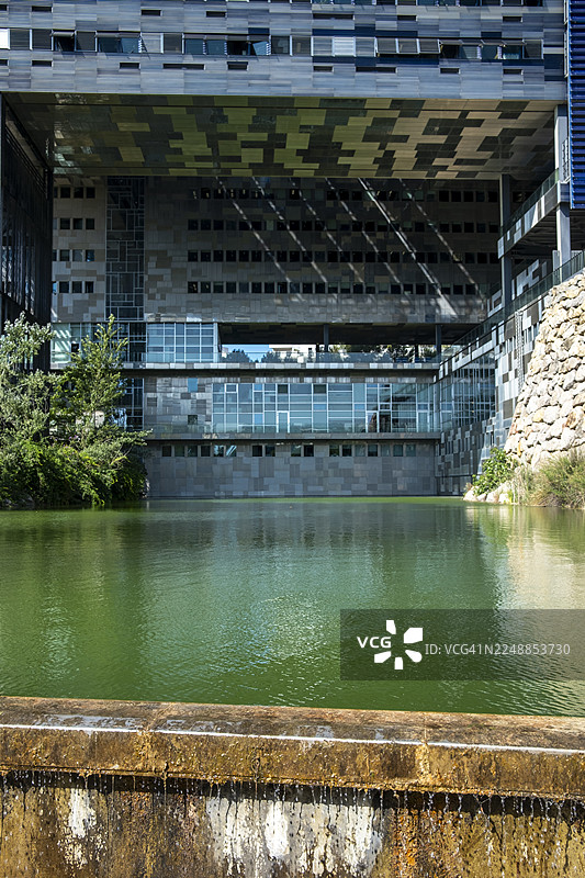 蒙彼利埃市政厅下部结构倒映在水面上，水面位于其伸出体量和石砌堤岸下方图片素材