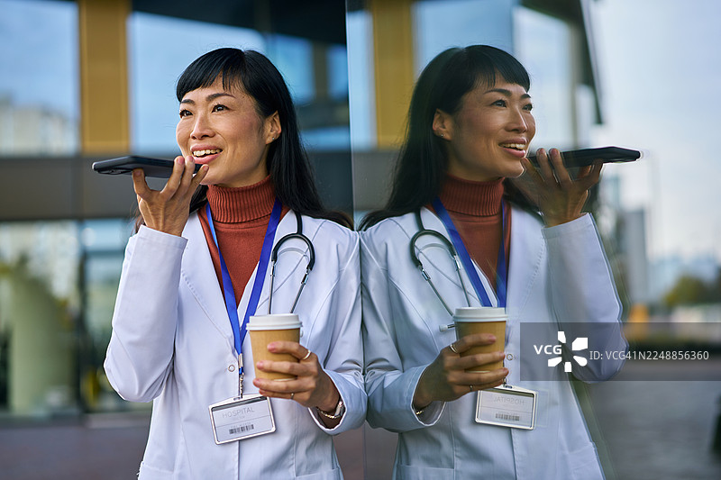 亚洲女性医生用智能手机发送语音消息图片素材