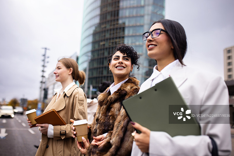 年轻的职业女性在上班途中，手持咖啡和平板电脑，走在柏林街头图片素材