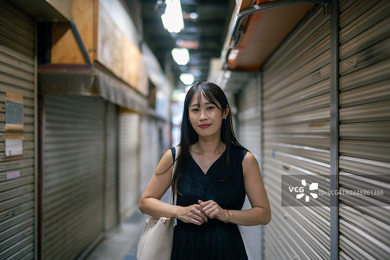 身穿黑色连衣裙的女子肖像，站在一条狭窄的购物街上，所有店门都已关闭图片素材