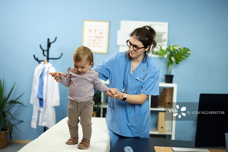 儿科医生在体检时帮助女婴学走路图片素材