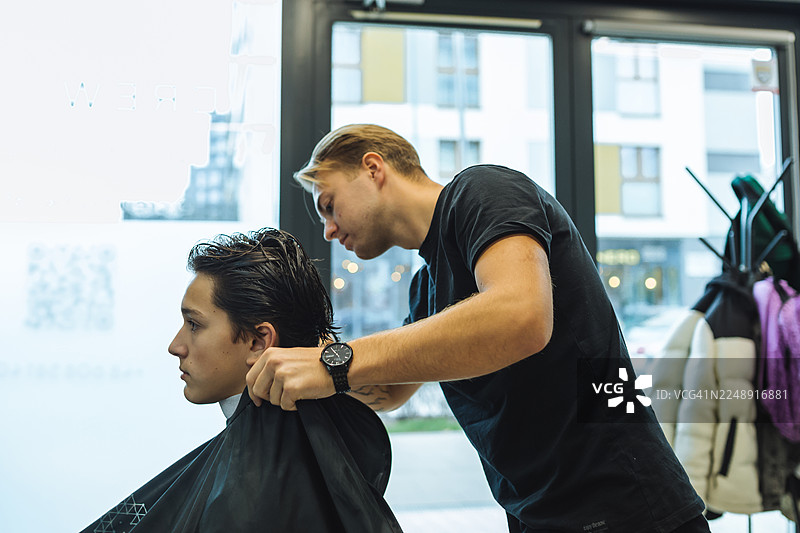 时尚青年在现代理发店理发，理发师专注地工作图片素材
