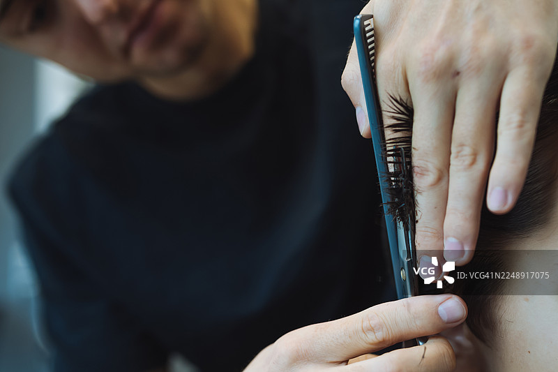 理发师在现代理发环境中，用剪刀和梳子精确地近距离修剪侧面头发，展现了细致的造型工作、发质纹理和专注的技巧。图片素材