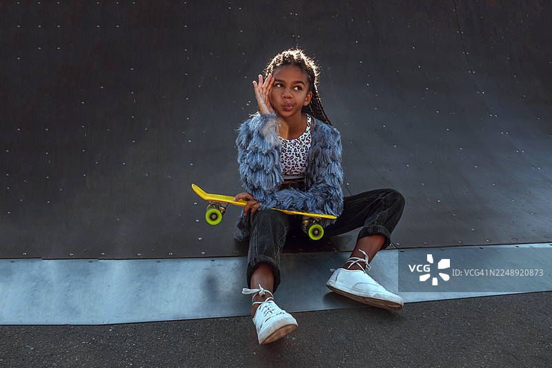 一个皮肤黝黑的女孩在斜坡上玩滑板。一项青少年积极的娱乐活动。图片素材