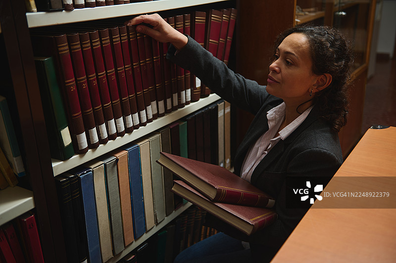 专注的女性在安静的图书馆学习时，伸手去拿书架上的书图片素材