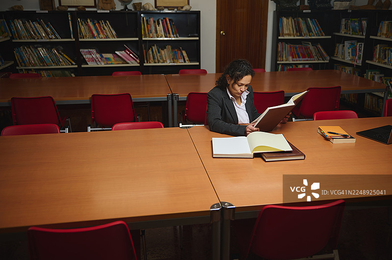 职业女性在图书馆的大会议桌旁，被书籍环绕着学习图片素材
