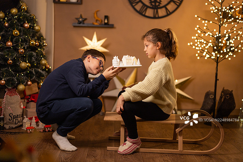 孩子们在舒适的客厅里，装饰好的圣诞树旁边的雪橇上玩着微型圣诞村庄图片素材