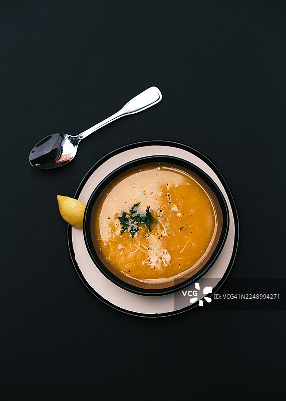 传统土耳其鸡肉汤的俯视图，盛在黑色碗中，配有肉丝和清淡的调味料，旁边放着现代盘子里的新鲜柠檬角，舒适食物概念，适用于餐厅菜单、烹饪设计和正宗餐饮视觉效果。图片素材