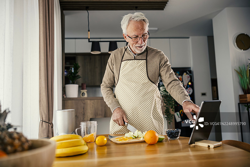 一位年长男性正在按照网上的食谱准备健康的果昔图片素材