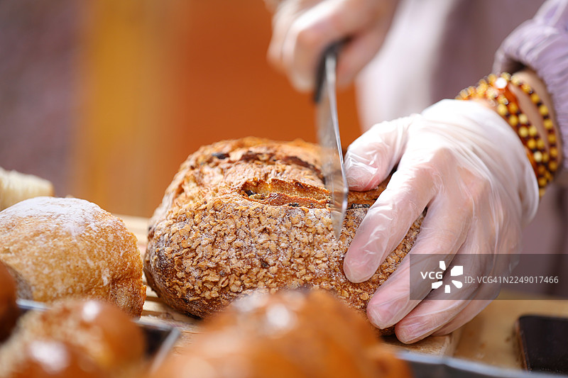 特写烘焙师的手在切板上切割刚出炉的全麦面包图片素材