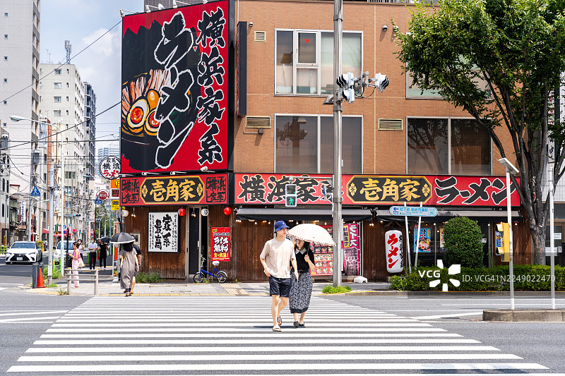 一对情侣在东京一家拉面店前穿过繁忙的街道图片素材