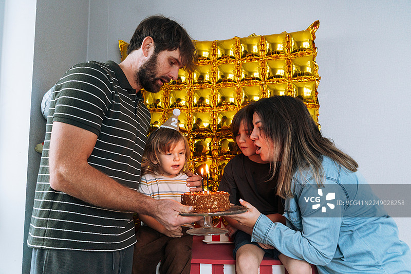 温馨的家庭在家中庆祝二岁生日，可爱的幼儿正在吹灭生日蛋糕上的蜡烛图片素材