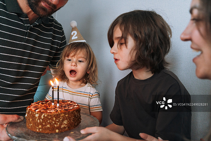 快乐的一家人在家庆祝二岁生日，可爱的小孩在生日蛋糕前吹蜡烛图片素材