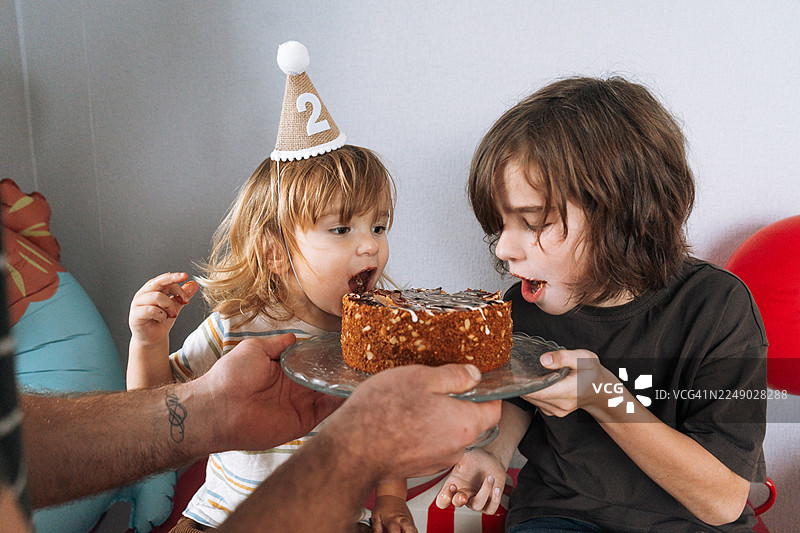 搞笑的弟弟们在庆祝生日时咬蛋糕，可爱的脏兮兮的孩子们享用巧克力甜点，童年时刻图片素材