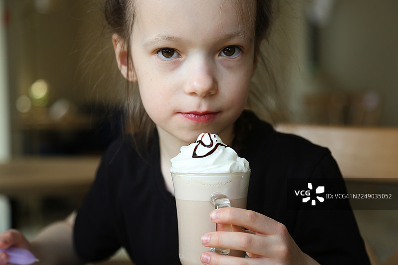 8岁小女孩在当地咖啡馆放松，喝着加奶油的热巧克力，并看向镜头图片素材