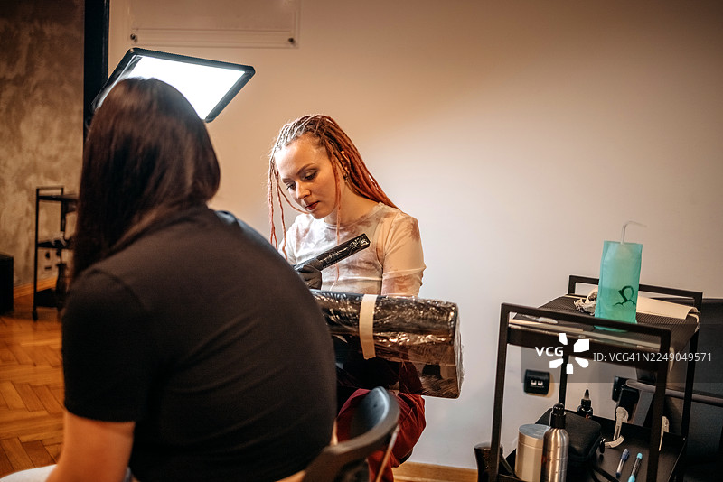 女纹身师在纹身店为顾客的手臂纹身图片素材