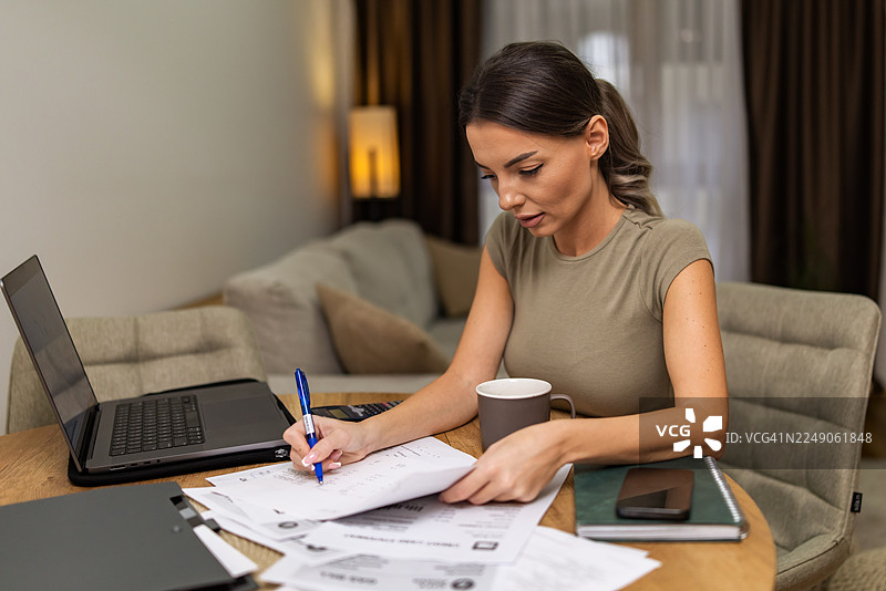 一位迷人的女性在家中办公室处理文件并进行分析。图片素材