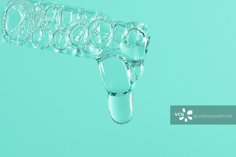 透明玻璃滴管特写，滴有蓝绿色液体，背景为柔和的粉色，适用于健康、科学和养生项目的抽象医学与科学概念图片素材