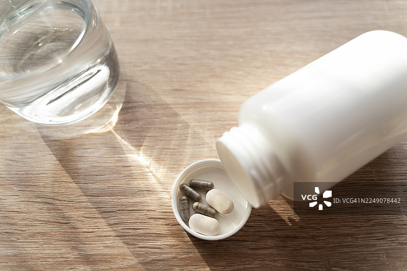 瓶盖里的药片和补充剂，旁边放着一杯水，置于木质表面上图片素材