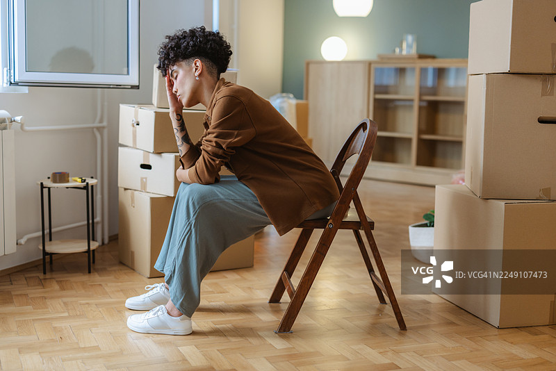 一位年轻女子坐在部分打包的房间里，在搬入新公寓时陷入沉思，表情担忧图片素材
