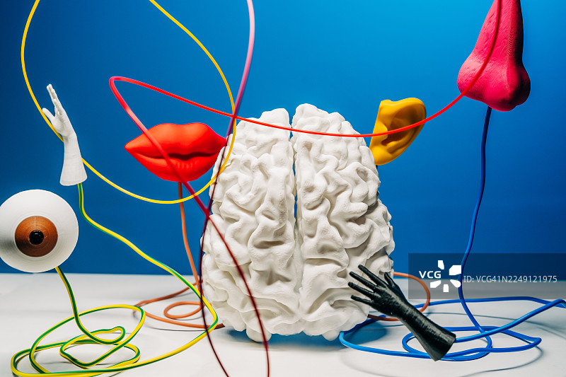 一幅超现实静物画，画面中有脱离的人体部位——眼睛、鼻子、嘴巴、耳朵和手，它们被固定在彩色的线上，背景是鲜艳的蓝色。图片素材