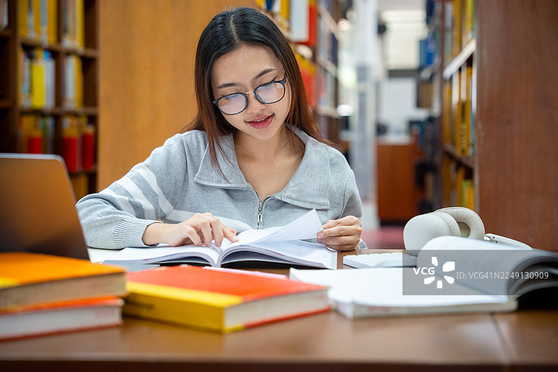 教育与学校概念。年轻女子在图书馆读书。漂亮的亚洲女大学生微笑着抱着书坐在图书馆里。学习与教育图片素材