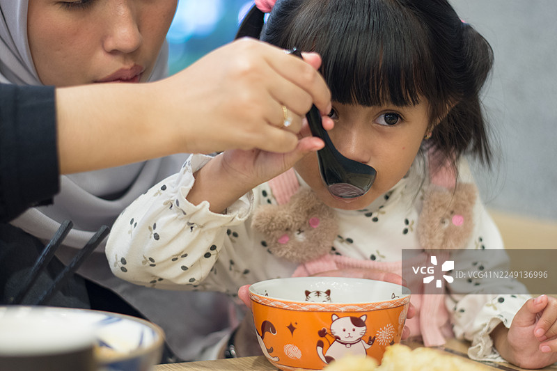 穆斯林母亲喂亚洲式面条汤给小女儿的特写图片素材
