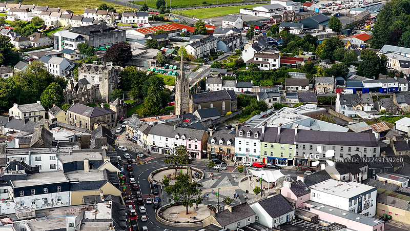 从空中俯瞰多尼戈尔郡多尼戈尔镇中心,这里有历史建筑、教堂、色彩鲜艳的店面和一个圆形公共广场,周围环绕着绿色山丘和乡村景观,体现了城市文化和旅游目的地概念。图片素材