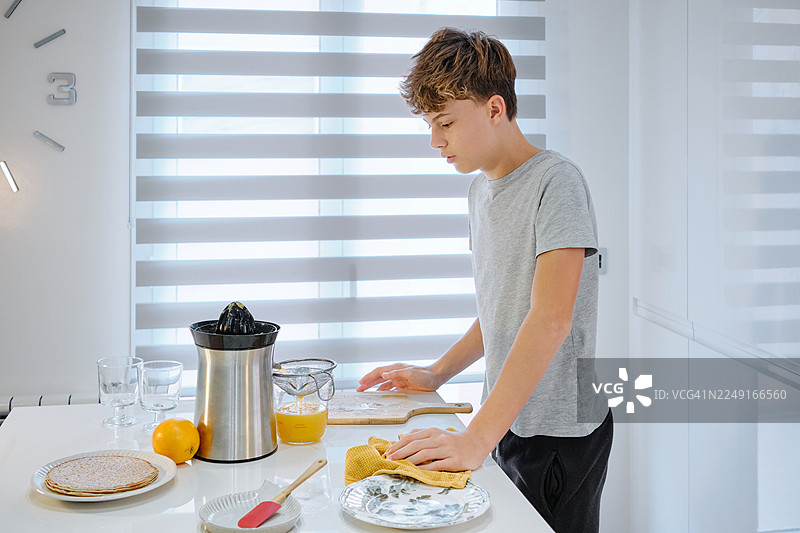 青少年在现代家庭厨房里榨新鲜橙汁图片素材
