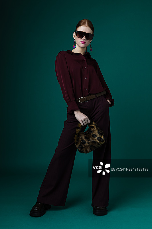自信的女性身着时尚酒红色服装，手持豹纹手提包自信摆拍图片素材
