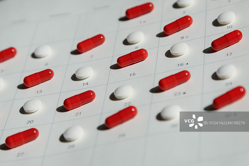 药品与医疗。红色铁质胶囊和白色止痛药丸并排排列在日历背景前图片素材