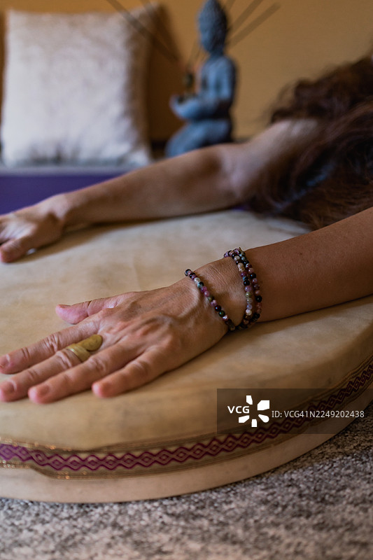 佛教、印度教和瑜伽概念。手持念珠的女性手部特写，背景为皮革鼓和佛陀像。图片素材