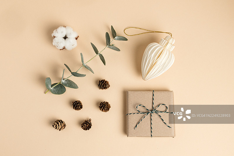 极简圣诞节平铺摄影，背景为米色，包含棉花、桉树和礼品盒图片素材