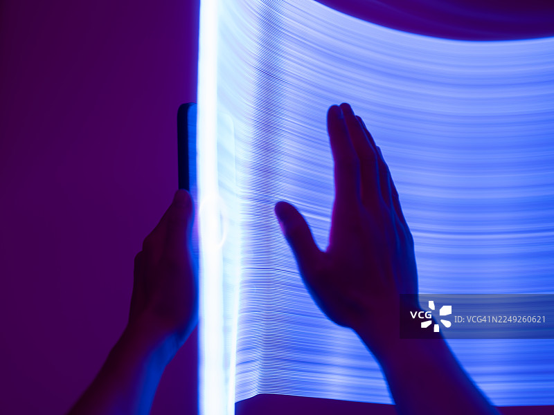 特写一只手握着智能手机。长曝光和LED光绘。科技与人工智能的概念。图片素材