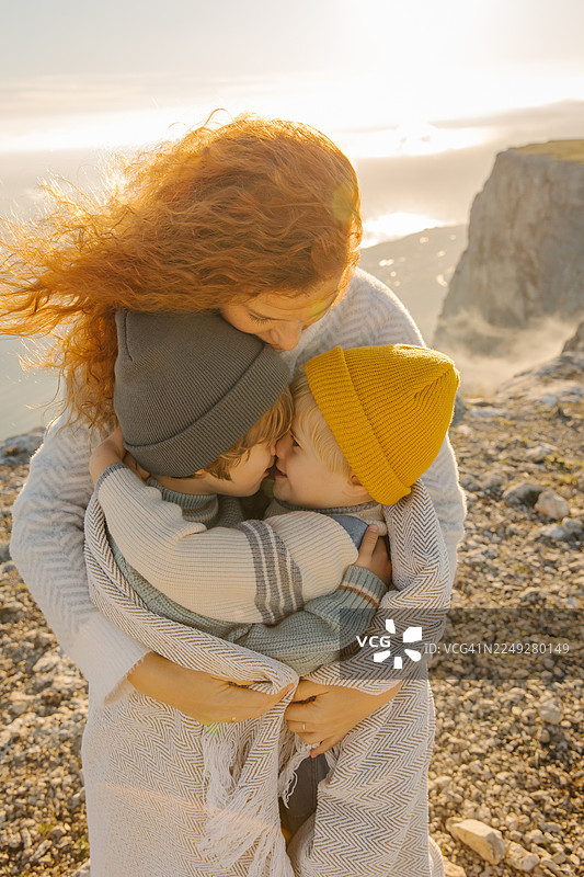 夕阳下悬崖边，母亲在海风中拥抱两个孩子图片素材