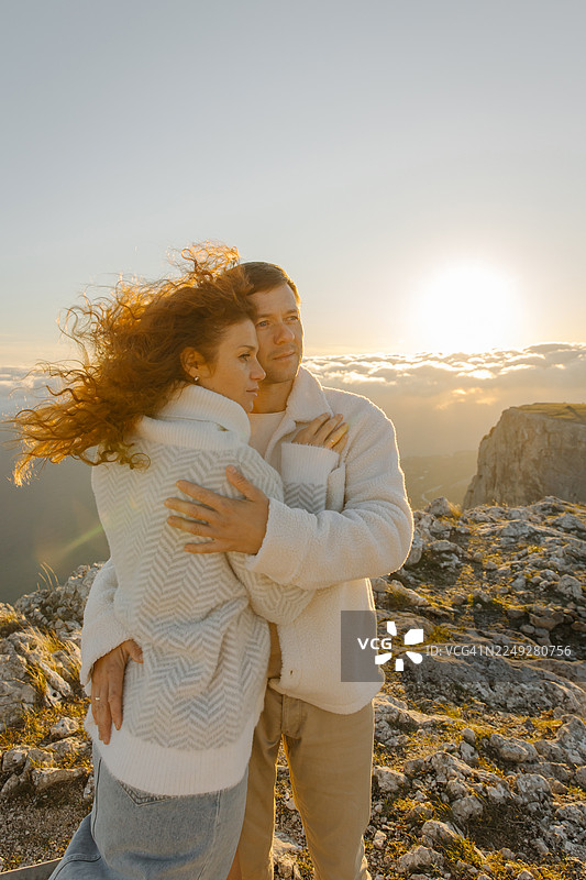 情侣在山脊上拥抱，沐浴在日落的余晖中，身穿舒适的白色毛衣图片素材