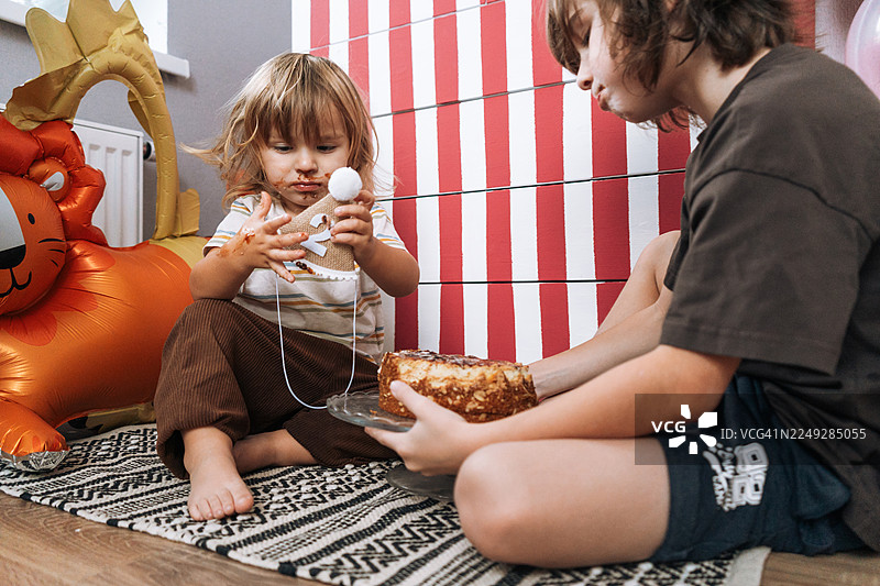 有趣的弟弟们在庆祝时啃咬生日蛋糕，可爱的弄脏了嘴的孩子们吃着巧克力甜点，童年时光图片素材