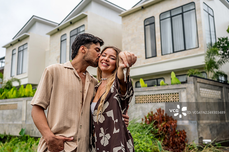 情侣手持钥匙，在现代住宅前庆祝乔迁之喜，温馨浪漫的时刻图片素材