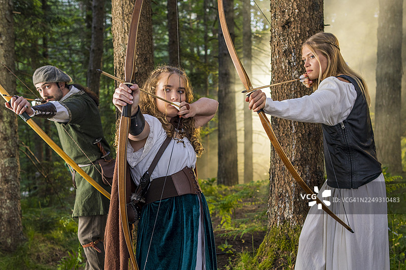 中世纪年轻弓箭手在森林中展示他们使用弓的专注和技巧图片素材