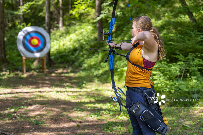 一名十几岁的白人女孩在森林中专注练习射箭图片素材