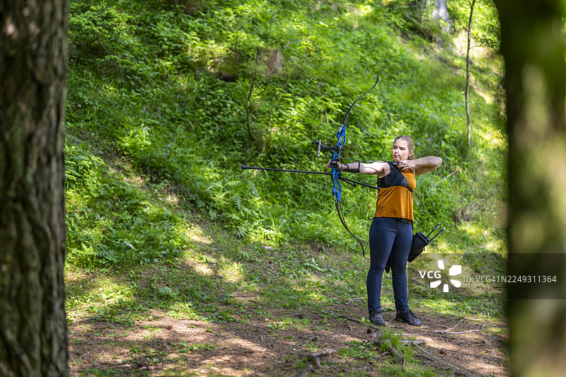 阳光明媚的森林空地上，一位青少年白人女孩正在练习射箭图片素材