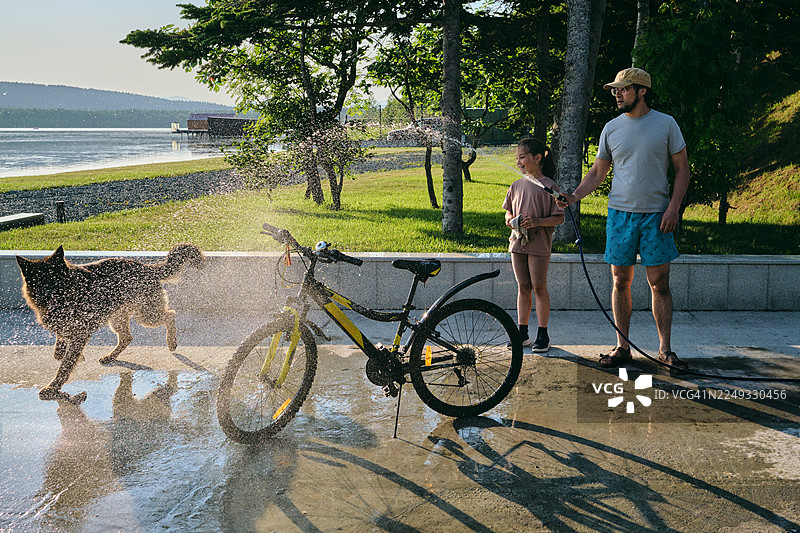 一位父亲和他的女儿正在用软管清洗自行车，为骑行季做准备。图片素材