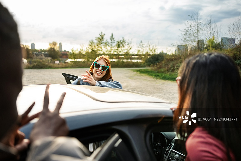 年轻女子兴高采烈地在车旁与朋友聊天图片素材