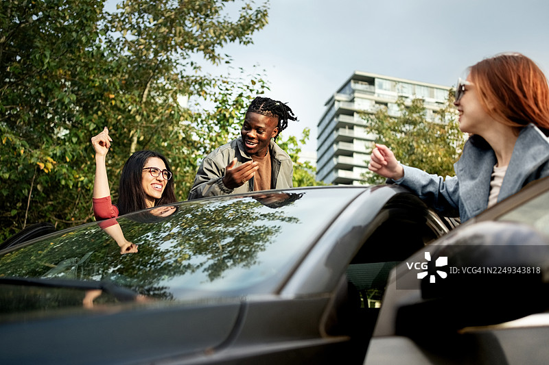 三个快乐的朋友们靠在户外的一辆车旁图片素材